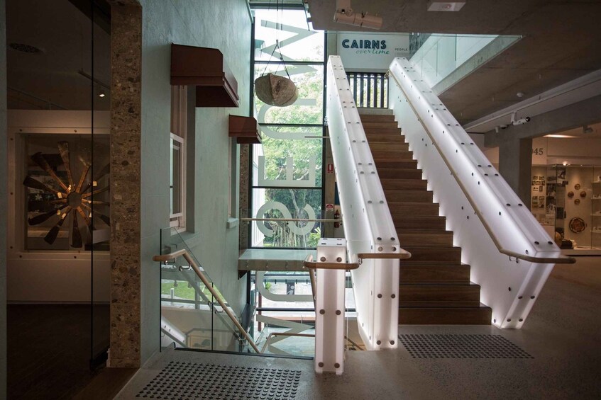 A modern interior with a glass staircase, a hanging basket, and a sign reading 'CAIRNS evertime.' 2
