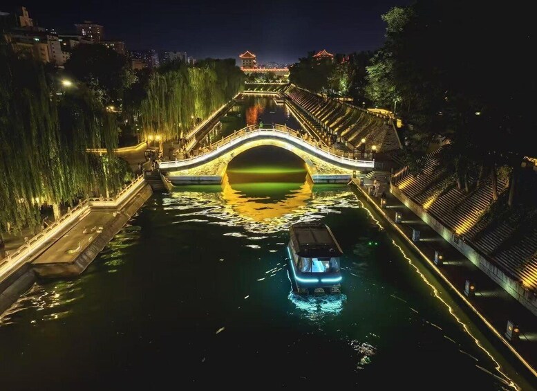 A lit bridge over water with a boat in the middle, surrounded by trees and buildings. 4