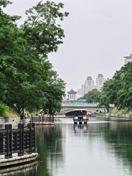 A calm river with a traditional boat, a bridge, and modern buildings in the background. 5