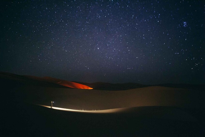 A desert landscape at night with a person standing on a dune, illuminated by a flashlight. 1