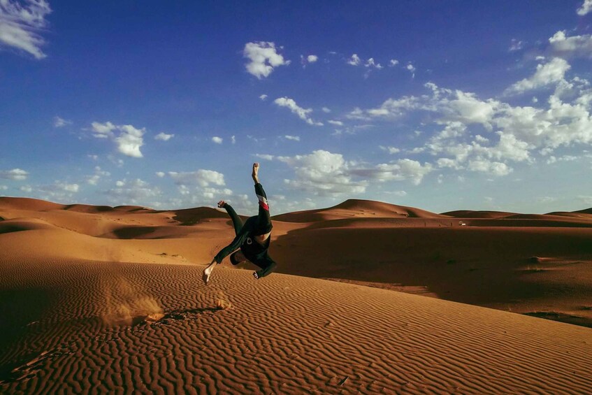 A person performing a backflip in a desert landscape with sand dunes and a clear sky. 2