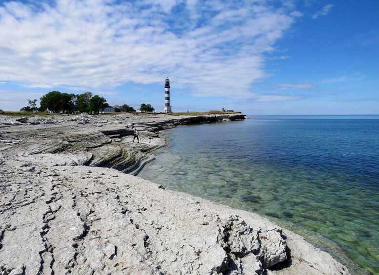 A rocky shoreline with a lighthouse in the distance and clear blue water. 3