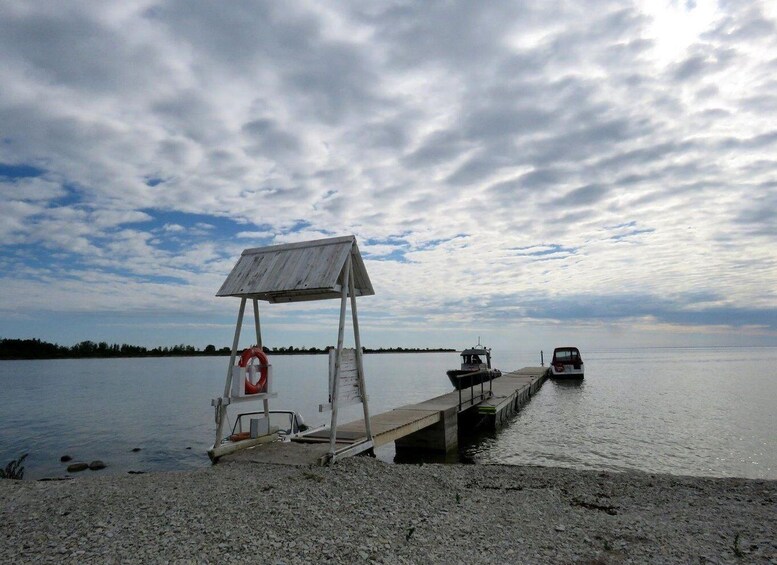 A dock with a lifebuoy, a small boat, and a car on a calm lake with a cloudy sky. 5