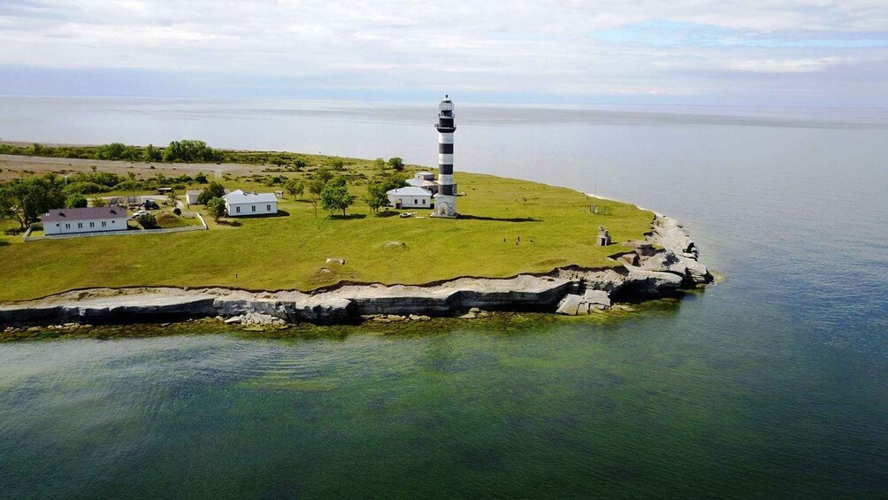 A lighthouse on a grassy island with a clear view of the water and a distant shoreline. 1