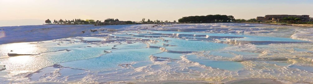 Terraced pools of mineral-rich water, a distant shoreline, and a large building. 1