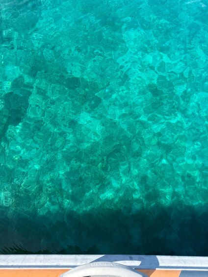 A clear turquoise pool with visible underwater rocks and a boat edge. 4