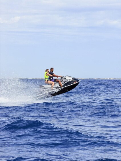 Two people jet-skiing on a body of water with a distant shoreline. 1