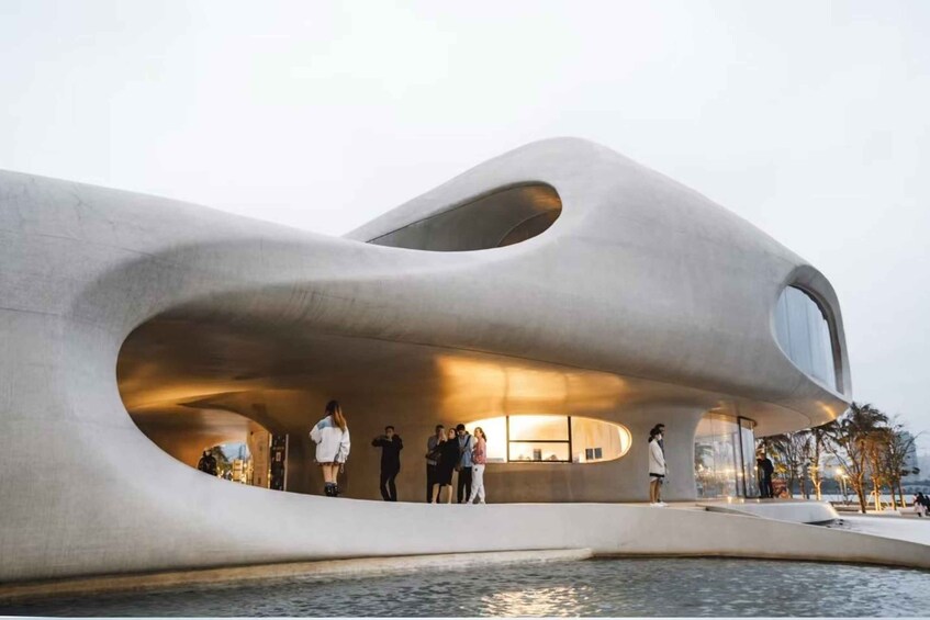 A modern architectural structure with a unique curved design, a reflective water body in front, and people gathered around. 4