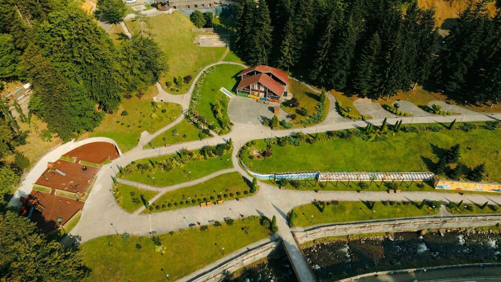 An aerial view of a park with a red-roofed pavilion, winding pathways, and a bridge over a river. 4