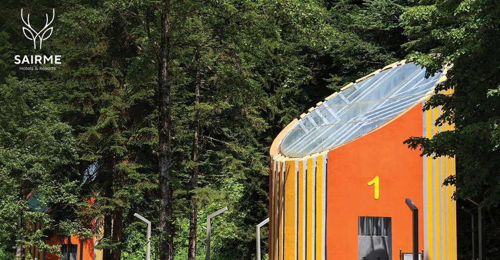 A building with a yellow and orange facade, surrounded by dense green trees. 2