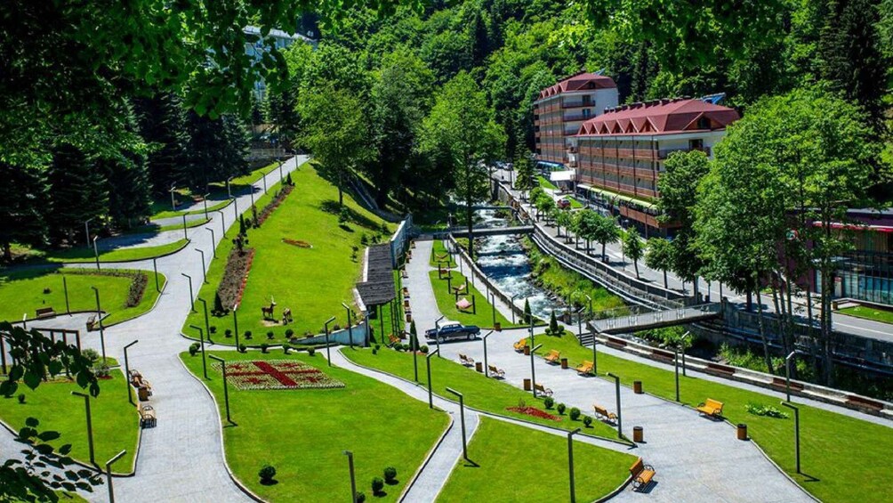 A park with a river, pathways, benches, and a building with a red roof. 5