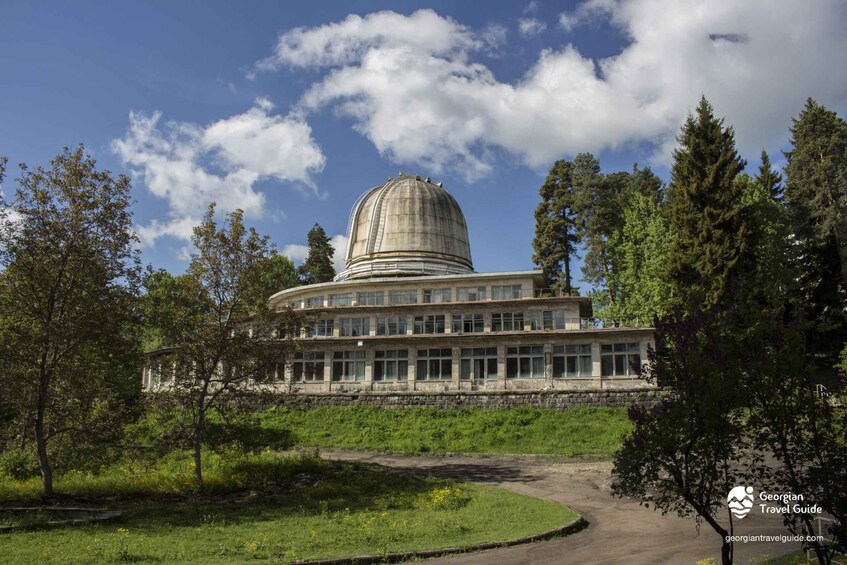 A large, domed building surrounded by trees and a clear sky. 5