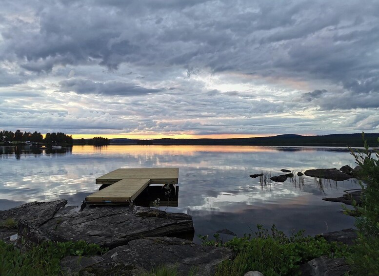 A calm lake at sunset with a wooden dock and rocks in the foreground. 2