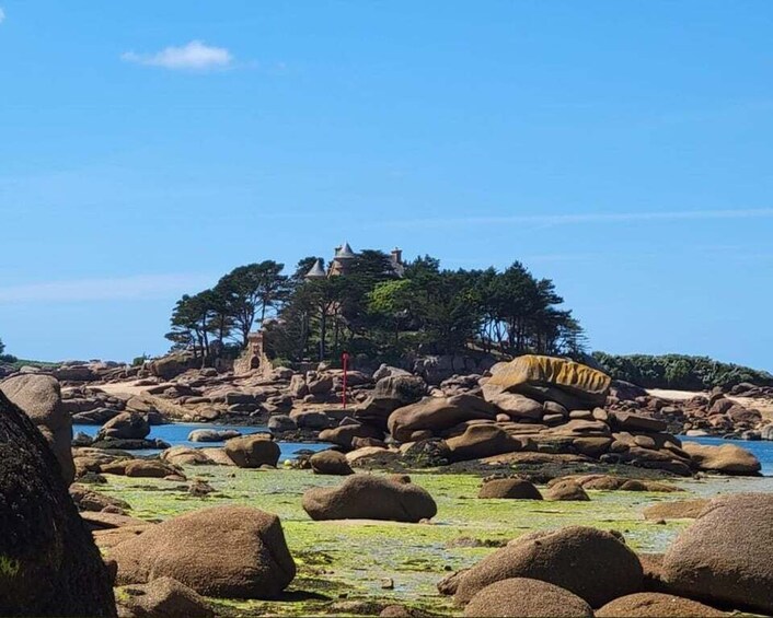 A rocky shoreline with large boulders and a small structure on a hill. 4
