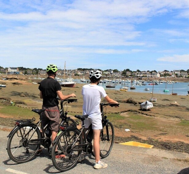 Two people on bicycles, a beach, and boats in the background. 3