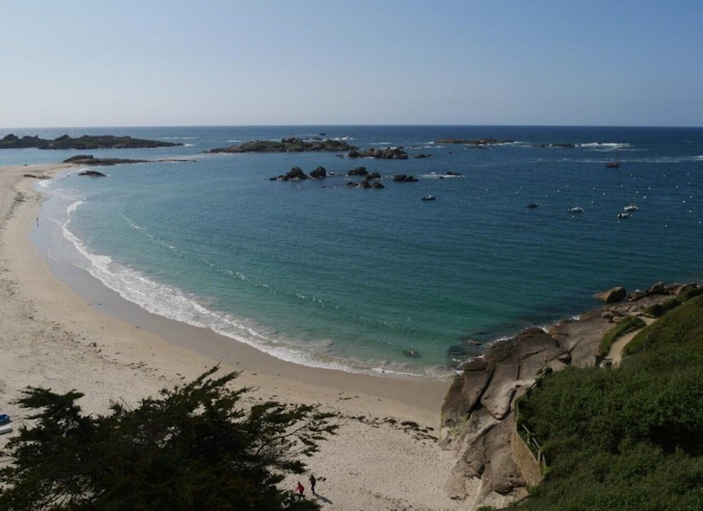 A coastal landscape with a sandy beach, calm sea, and rocky outcrops. 5