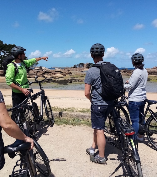 A group of cyclists on a coastal path with rocky terrain and a clear sky. 1