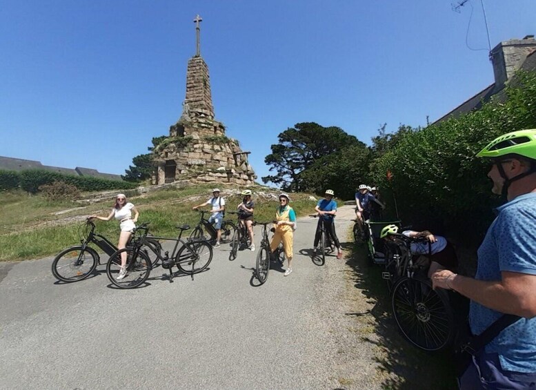 A group of cyclists on a road with a stone monument in the background. 2