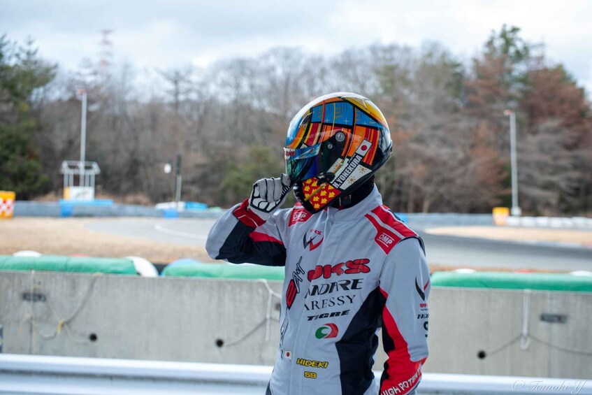 A person in a racing suit and helmet at a racetrack. 5