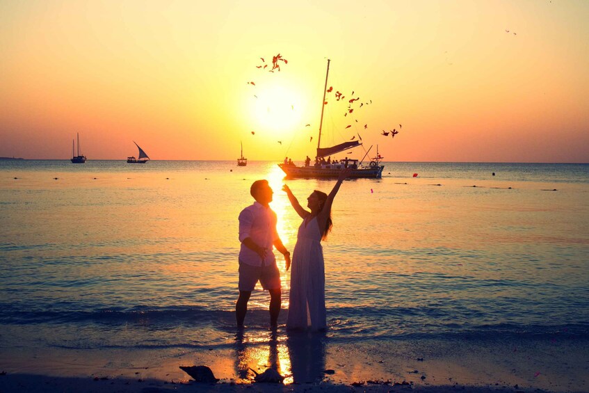 A couple standing on a beach at sunset with boats in the background. 4