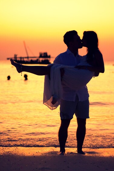 A couple embracing on a beach at sunset with a boat in the background. 1