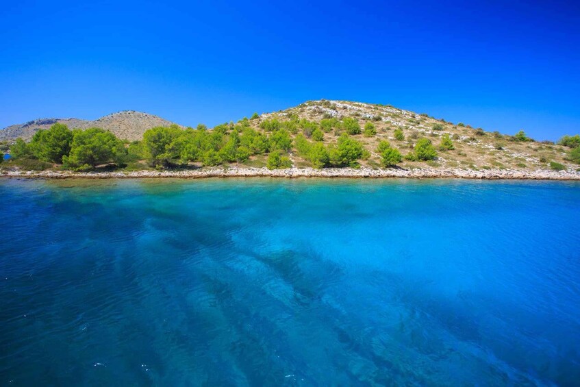 A coastal landscape with clear blue waters, a rocky shoreline, and a hill with sparse vegetation. 2