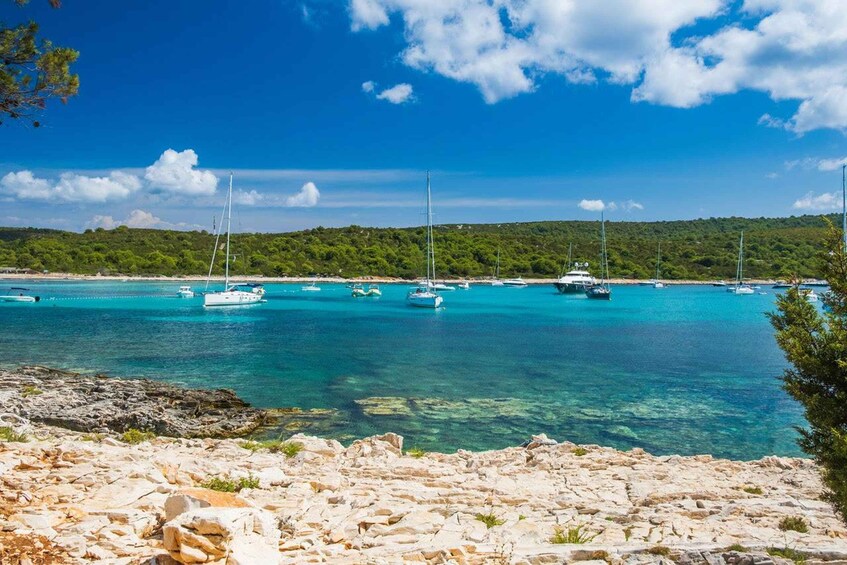 A coastal scene with clear turquoise waters, boats anchored, and rocky terrain. 3
