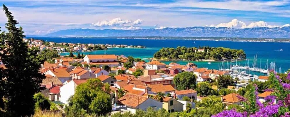 A coastal town with red-roofed houses, a marina, and a mountain range in the background. 4