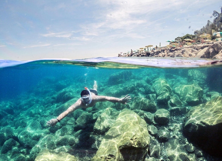 A person snorkeling underwater near a rocky shore with clear water. 3