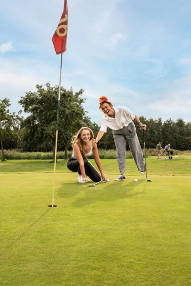 Two people on a golf course, one preparing to putt. 1