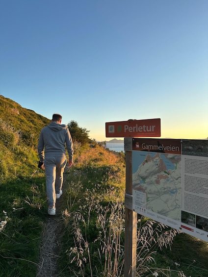 A man walking on a trail with a sign indicating 'Perleitur' and 'Gammelveien' in the background. 5