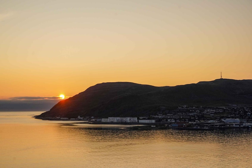 A sunset over a coastal town with a prominent hill and a radio tower. 1