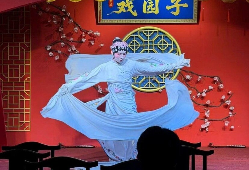 A performer in traditional attire on a stage with a red backdrop and a decorative window. 4