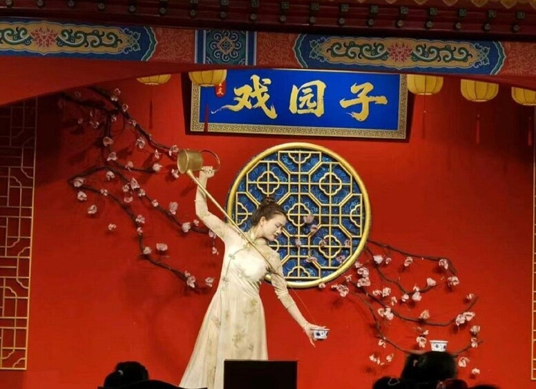 A performer in a traditional costume on stage with a red backdrop and a decorative blue sign with Chinese characters. 2