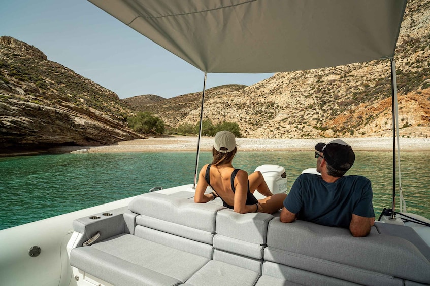 Two people on a boat with a rocky landscape and clear water in the background. 4