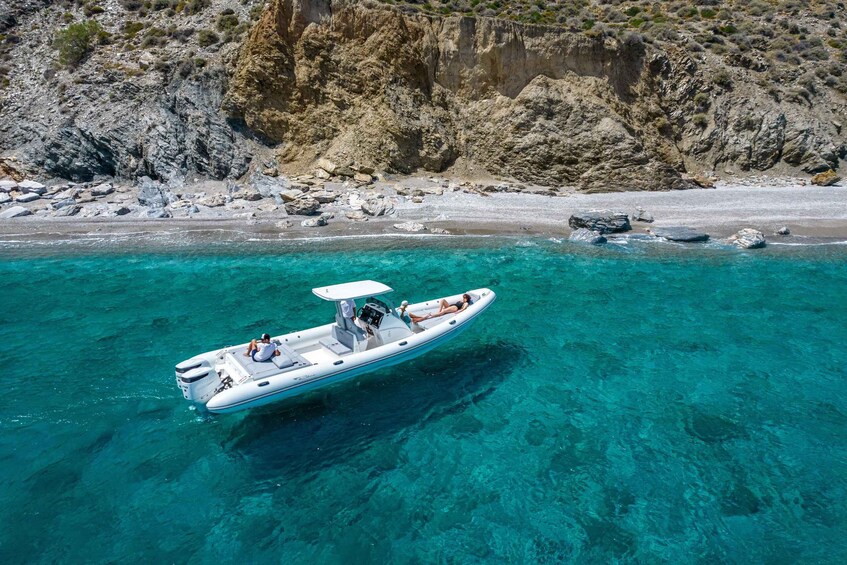 A white motorboat with two people on a clear turquoise sea, surrounded by rocky cliffs and a sandy beach. 2