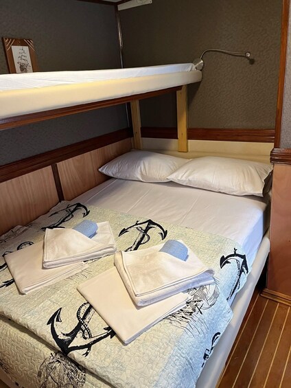 A bunk bed with a quilted bedspread featuring anchor designs, two neatly folded towels, and a picture frame on the wall. 3