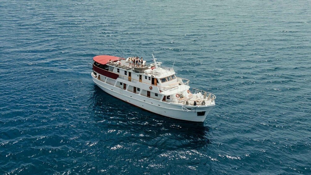 A white boat with a red deck and passengers on board, floating on calm blue water. 4