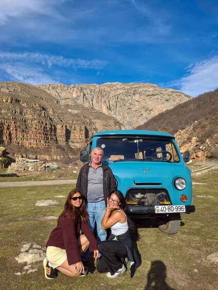Une voiture ancienne turquoise est garée sur un champ herbeux, avec une chaîne de montagnes en arrière-plan. 3