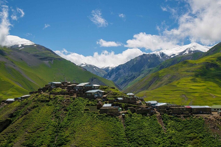 Un village de montagne, avec des maisons construites sur le flanc d’une colline, entouré de sommets enneigés et d’une végétation luxuriante. 1