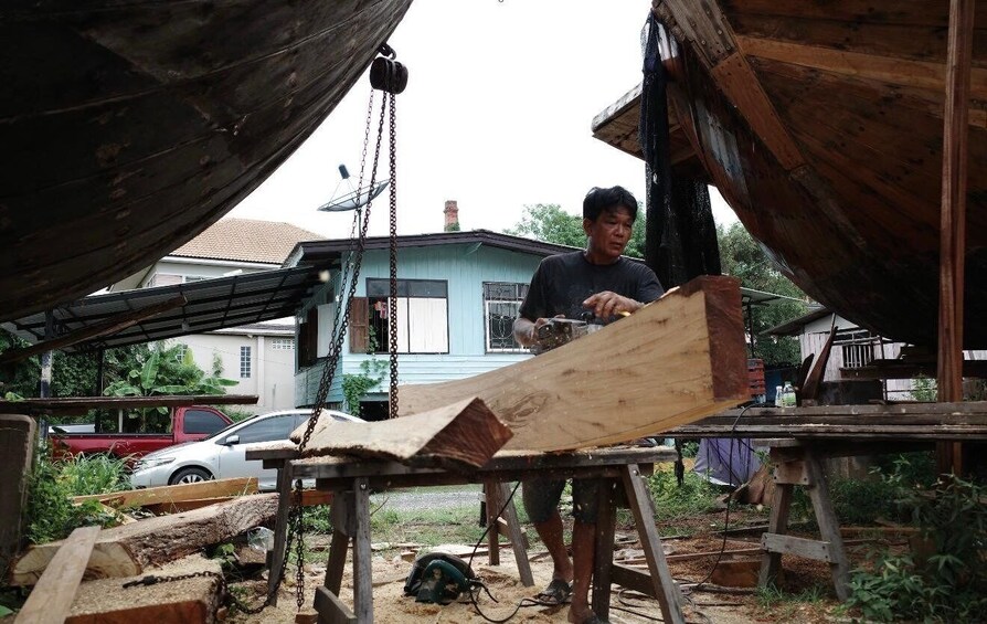 A person working with a large wooden plank outdoors, surrounded by construction materials and a blue house in the background. 5
