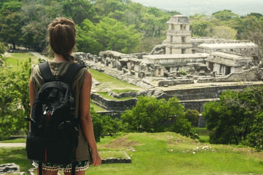 A person with a backpack overlooking ancient ruins surrounded by greenery. 1