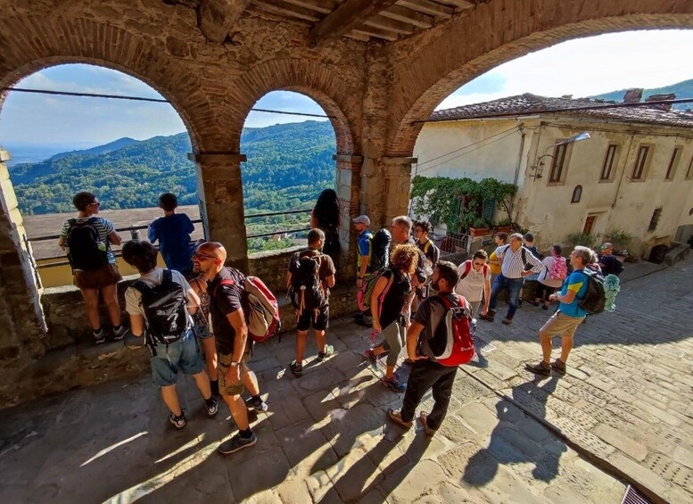A group of people standing and walking on a stone pathway with arches, overlooking a mountainous landscape. 1