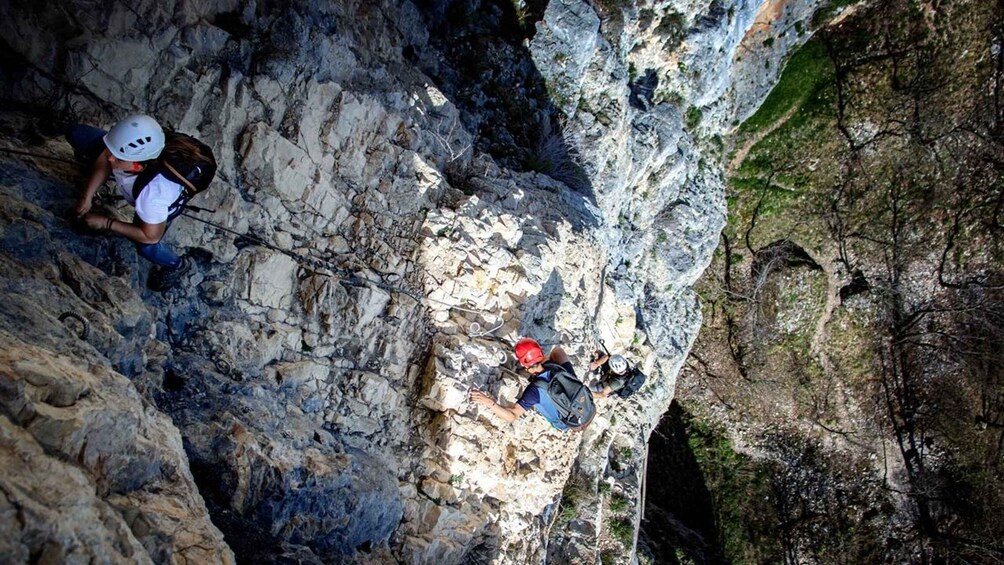 Two individuals rappelling down a rocky cliff with a narrow ledge. 3