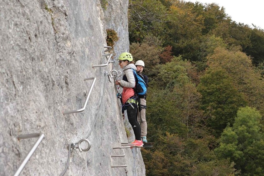Two individuals climbing a rock face with metal rungs. 1