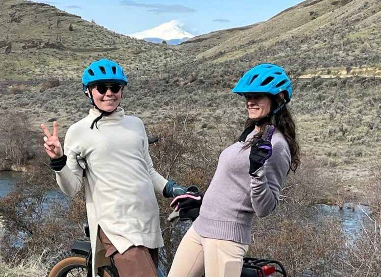 Two people on a mountain bike trail with a snow-capped mountain in the background. 1