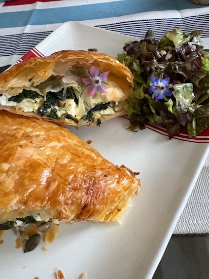 A pastry cut in half, revealing a spinach and cheese filling, served with a side salad. 2
