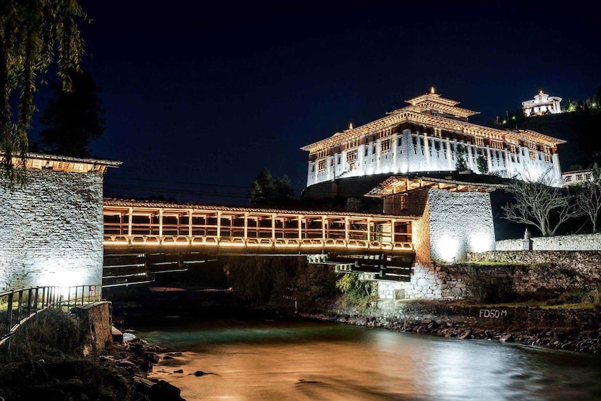 A lit bridge over a river at night, with a traditional building on a hill in the background. 3