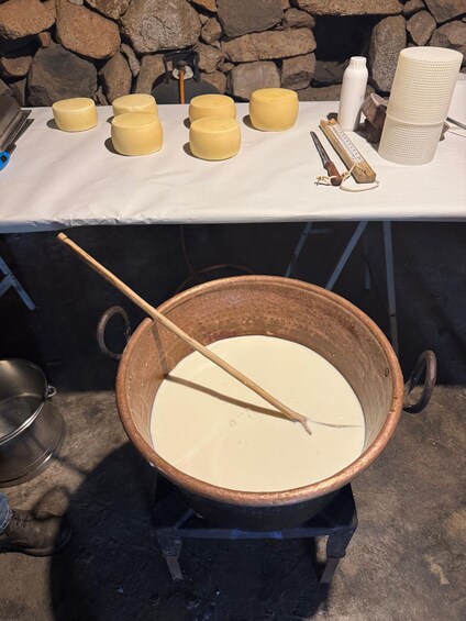 A large copper pot with a wooden spoon stirring a white liquid, surrounded by smaller containers and a white table with various items. 2
