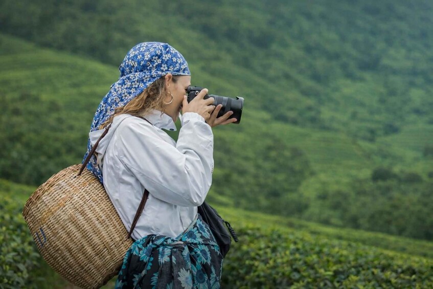 A person taking a photo with a camera, wearing a white shirt, blue floral headscarf, and carrying a woven basket. 3